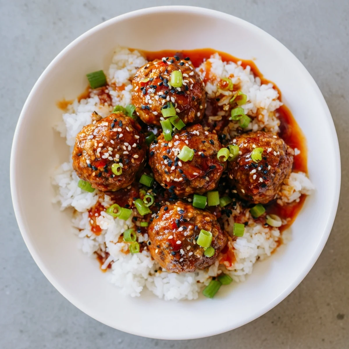 Tender Spicy Sriracha Beef Meatballs glistening with a vibrant glaze, served atop fluffy white rice.
