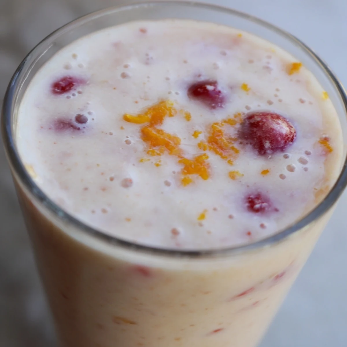 Vibrant red smoothie, the Cranberry Orange Smoothie with Yogurt, topped with zest and served with straws.