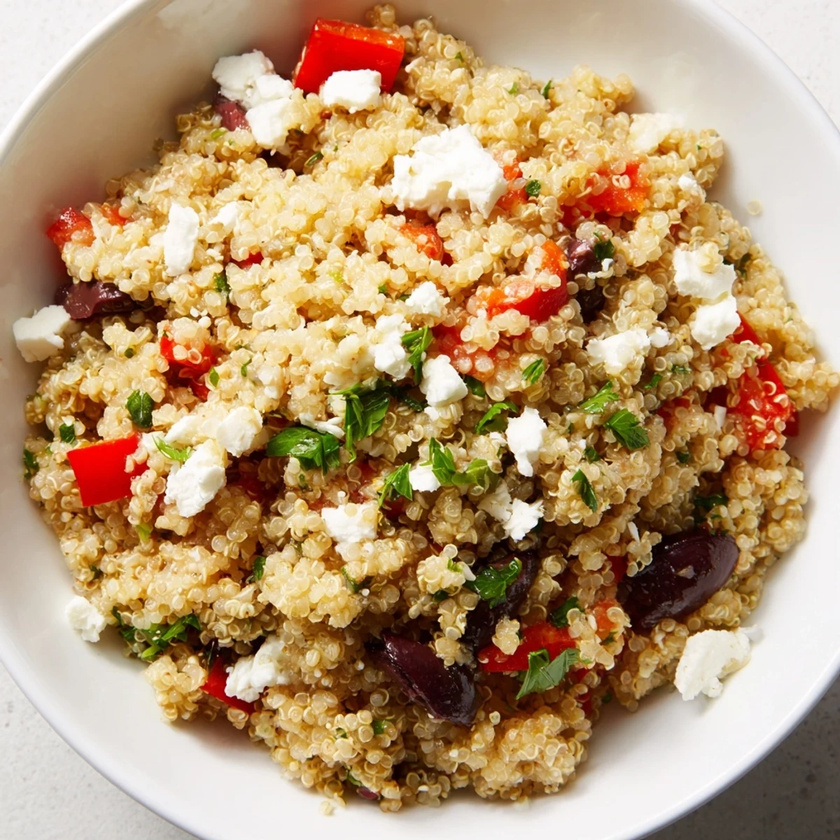 A colorful bowl of Mediterranean Quinoa Salad with Feta and Olives tossed with diced peppers and a lemony dressing.