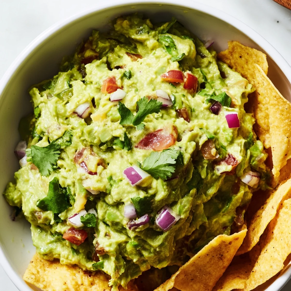 Freshly mashed avocado with diced jalapeño, red onion, and cilantro sits beside golden, crunchy tortilla chips, ready for a game day party.