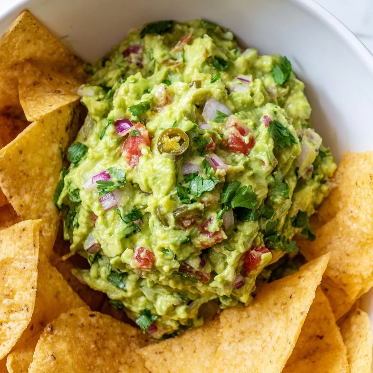 A bowl of Game Day Spicy Guacamole with Tortilla Chips features a zesty lime and cumin aroma, perfect for scooping during football season.