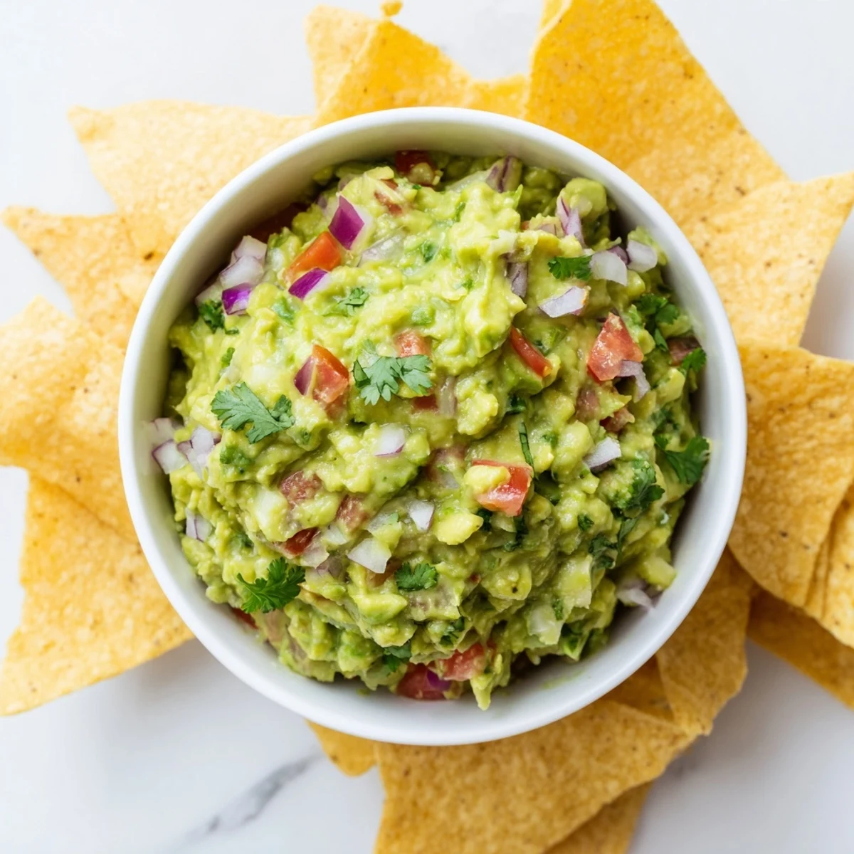 Close-up of homemade Game Day Spicy Guacamole with Tortilla Chips topped with tomato, offering a vibrant, gluten-free appetizer for any crowd.