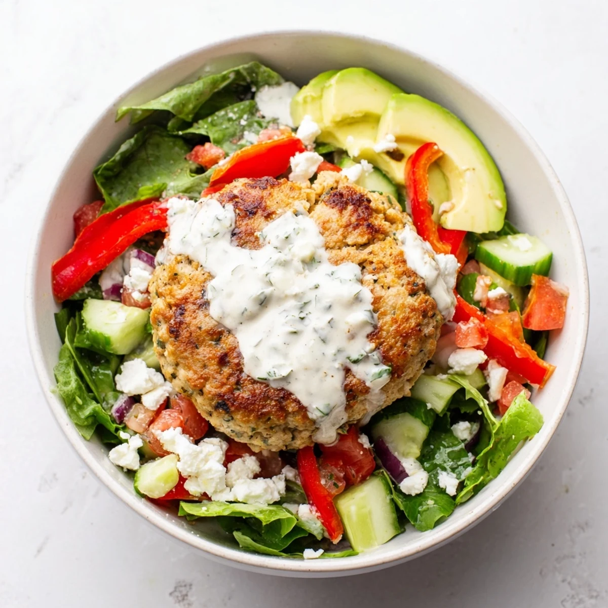 Golden, pan-seared turkey burger slices are arranged over fresh vegetables with crumbled feta and dill yogurt dressing in this complete salad bowl.