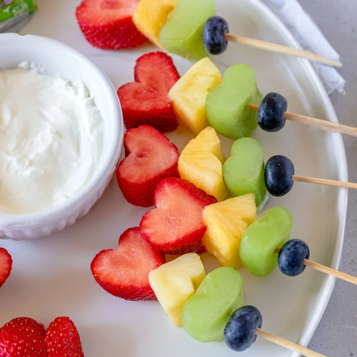 A close-up of Sweetheart Fruit Skewers with Yogurt Dip, showcasing honey-sweetened creamy dip alongside colorful melon and pineapple hearts.