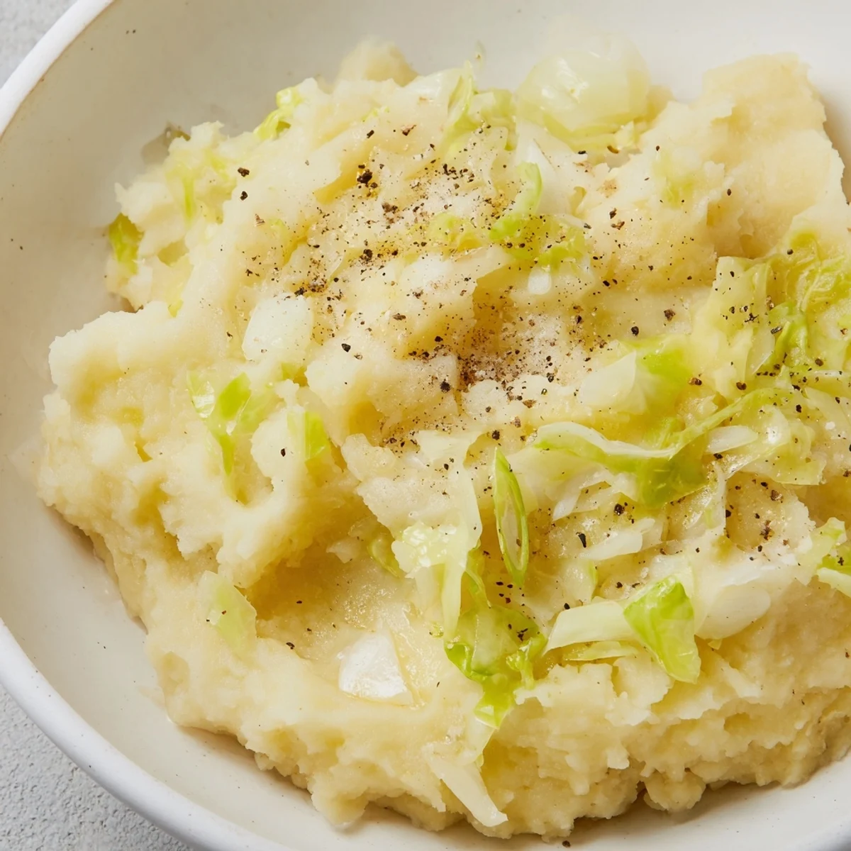 Creamy Irish Colcannon mashed potatoes with tender cabbage and green onions, topped with a melting pat of butter for a comforting side dish.