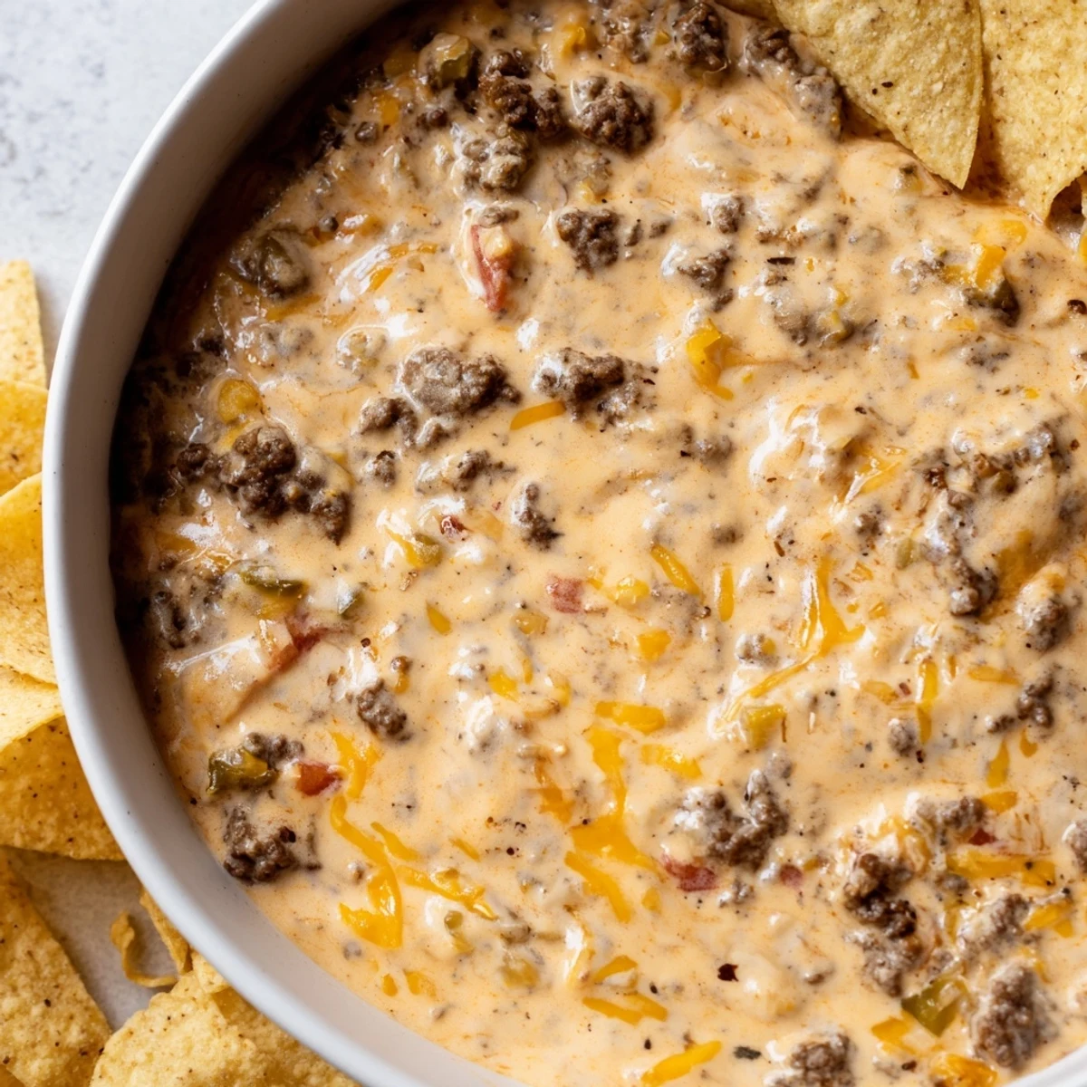 Savory Beef Queso Dip in a bowl, surrounded by crispy tortilla chips for dipping.