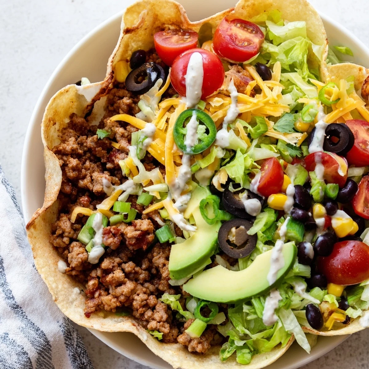 Hearty Tex-Mex salad featuring savory beef, jalapeño slices, black olives, and creamy avocado in a golden tortilla shell.