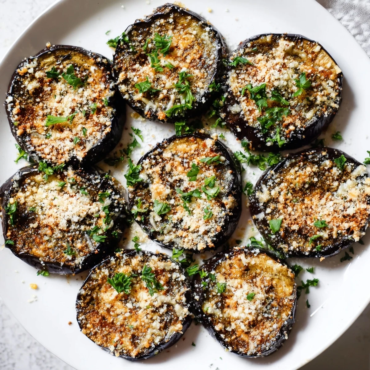 Roasted eggplant rounds with crispy Parmesan, Mediterranean herbs, and a squeeze of lemon for an easy vegetarian snack.  