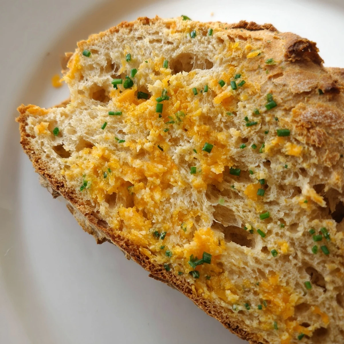 The Savory Cheddar & Chive Irish Soda Bread loaf has a golden crust with melted cheese bits, ready to slice and serve warm.  