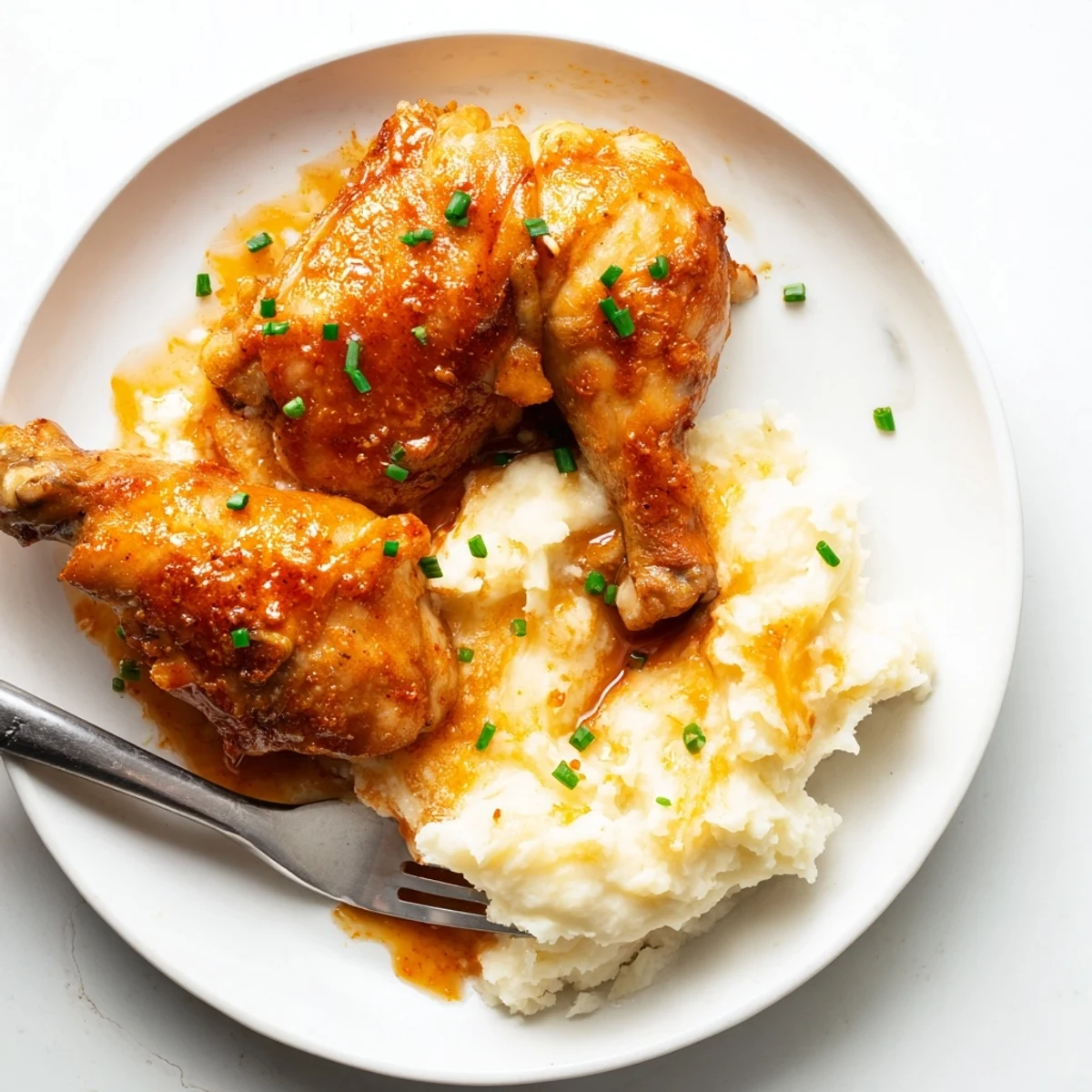 A close-up of chipotle honey chicken thighs alongside fluffy smoked Gouda potatoes, garnished with fresh chives.