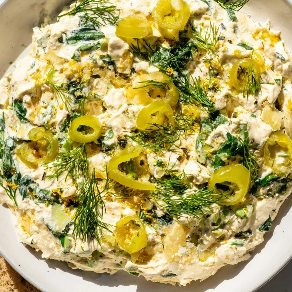 Creamy Spinach and Pepperoncini Baked Feta Dip topped with fresh dill, alongside sliced baguette for dipping.