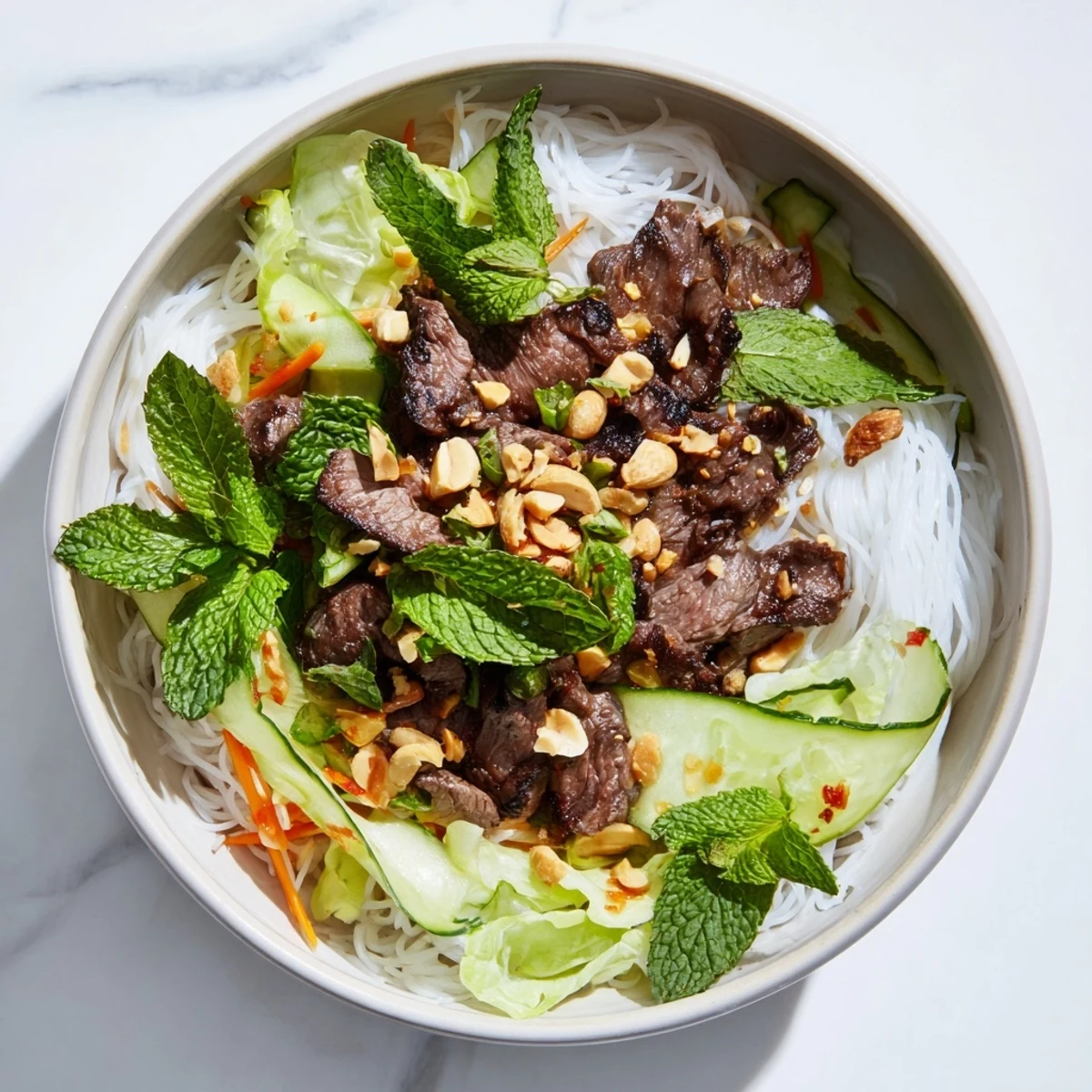 A vibrant bowl of Bun Bo Xao with sautéed beef, fresh herbs, and crisp vegetables on a table.