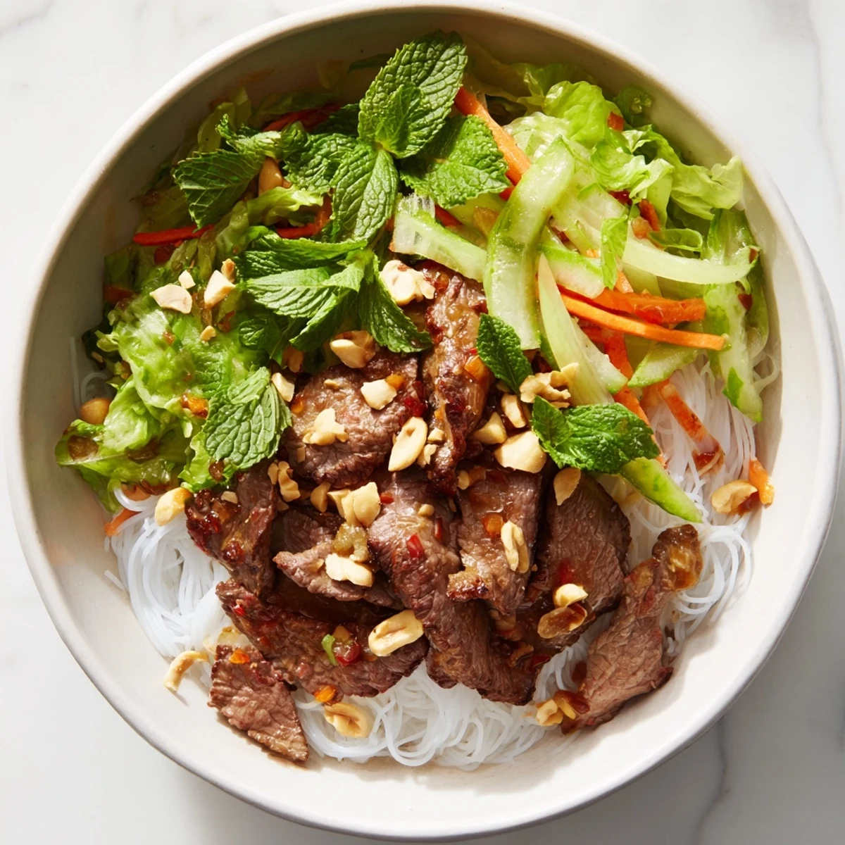 An overhead view of Bun Bo Xao ready to serve, garnished with peanuts and lime wedges.