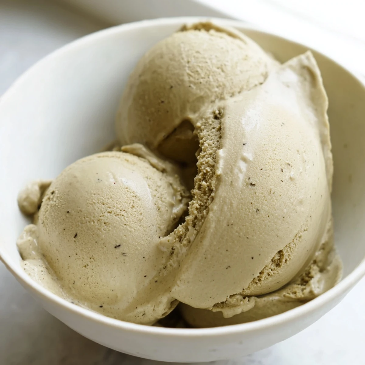 Rich, creamy Hojicha Ice Cream scooped into a bowl, topped with toasted sesame seeds and a swirl of black sugar syrup for a Japanese-inspired dessert.