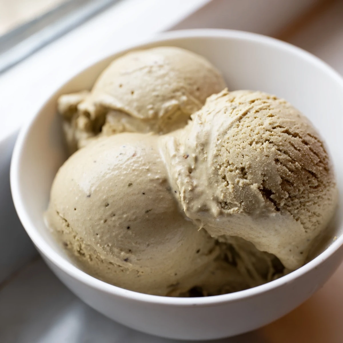 A close-up of scoops of Hojicha Ice Cream in a waffle cone, steam rising slightly from the freshly churned, nutty green tea dessert.