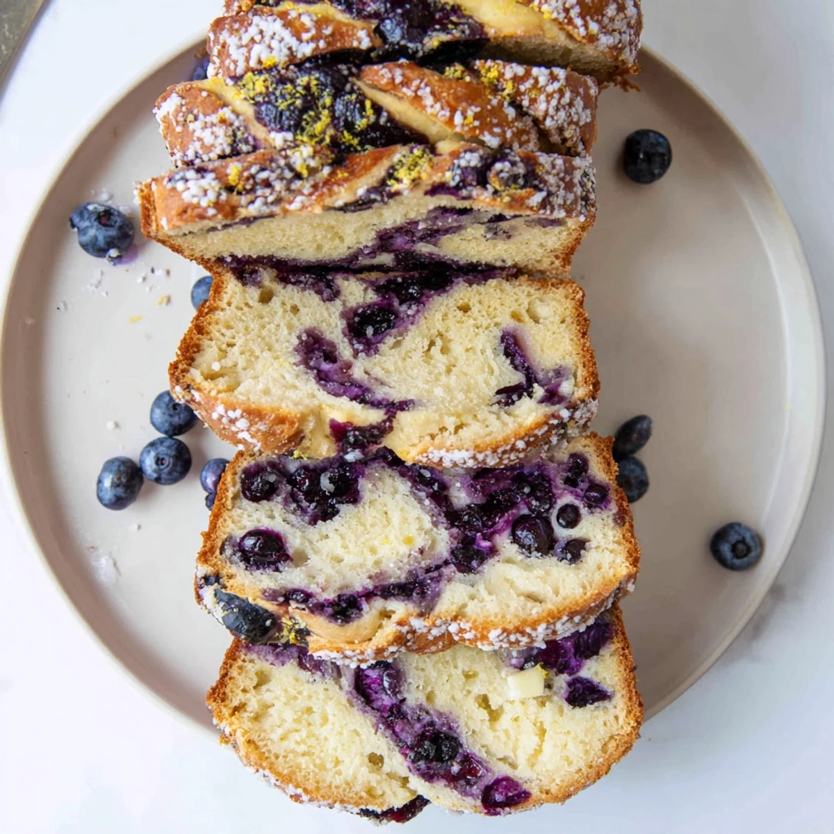 A golden Blueberry Lemon Cream Cheese Sourdough loaf sits on a rustic wooden board with fresh lemon zest scattered on top.