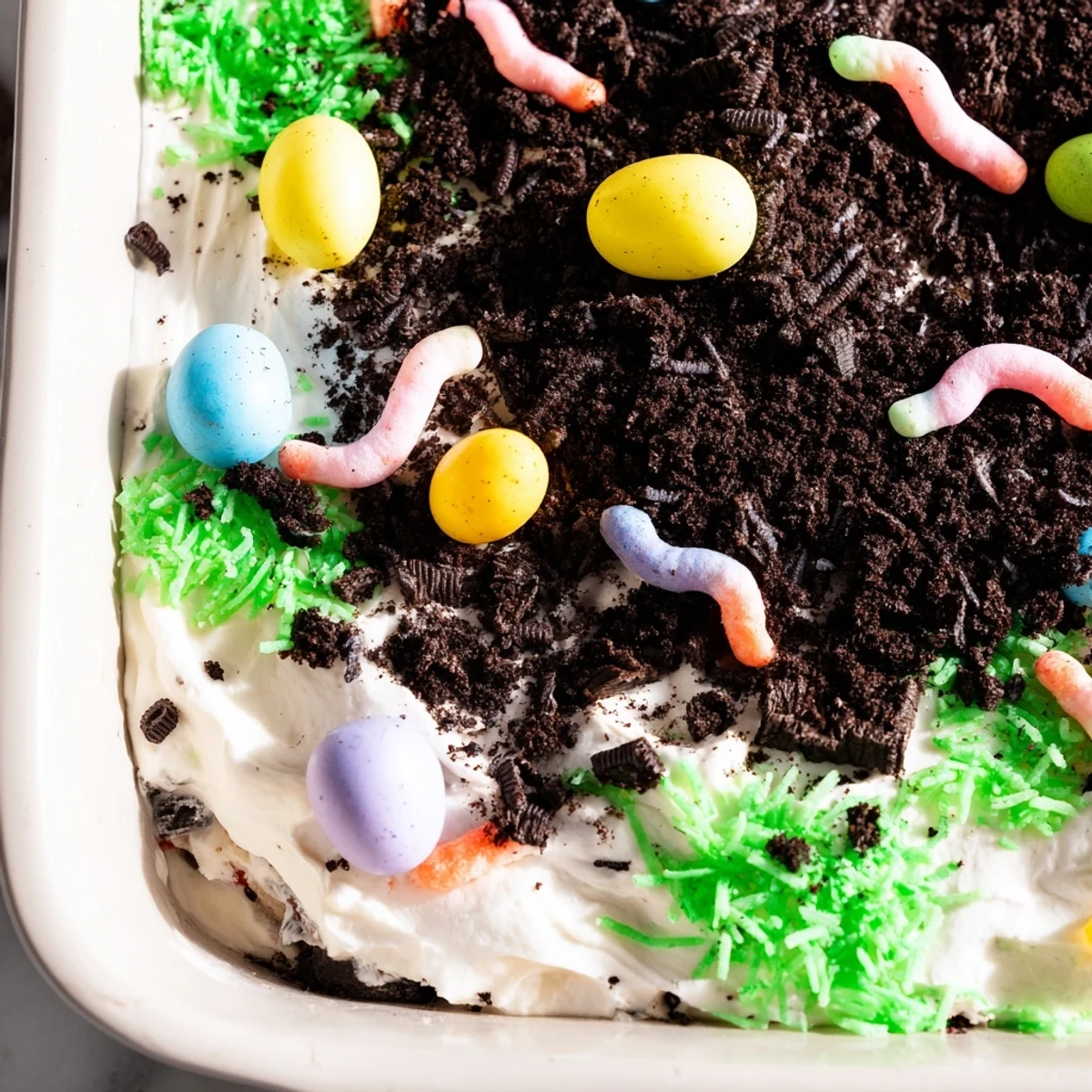 A close-up of Easter Dirt Cake Casserole with creamy layers, crumbled Oreos, and gummy worms on top.