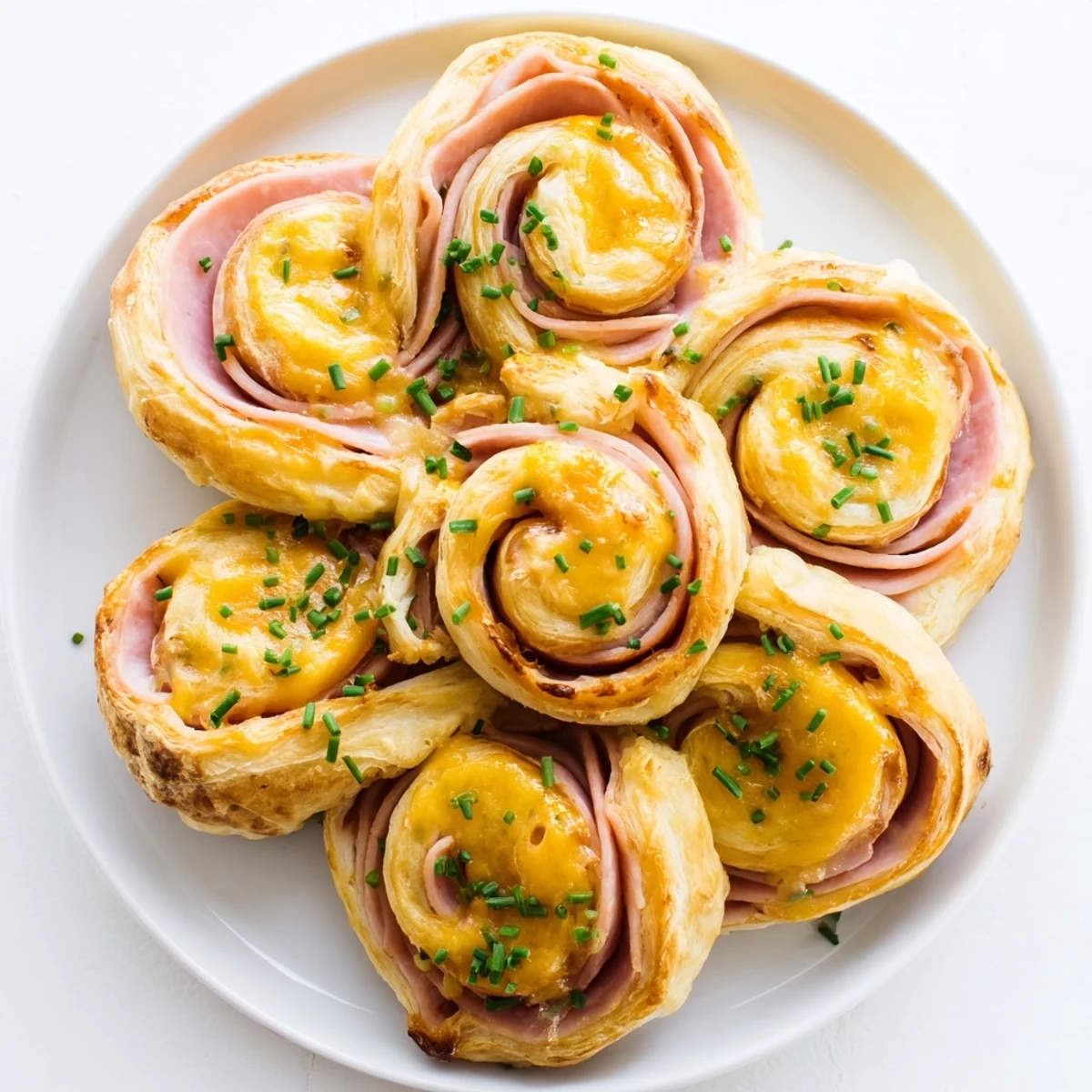 Golden-brown Easter Ham Cheddar Pinwheels cooling on a wire rack with fresh chives nearby.