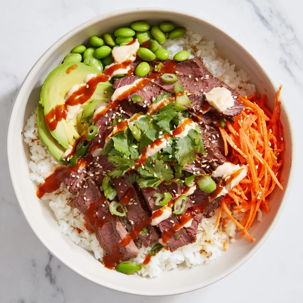 Sliced marinated flank steak draped over steamed rice with colorful vegetables and spicy mayo drizzle