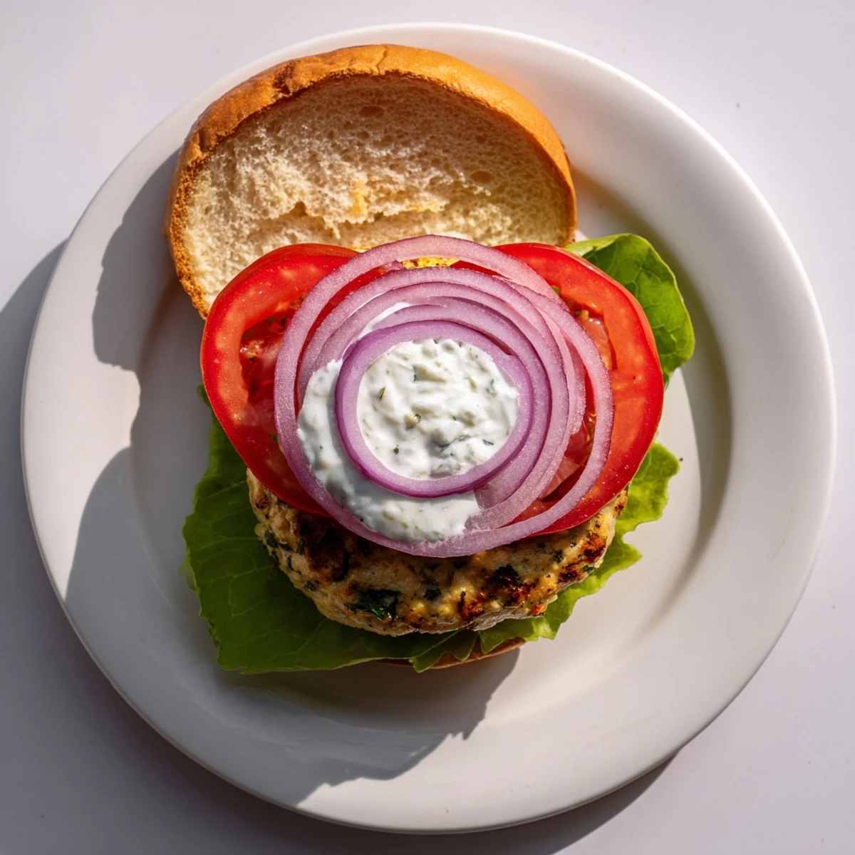 Golden brown Greek chicken burgers topped with fresh tzatziki sauce and crisp vegetables on toasted buns