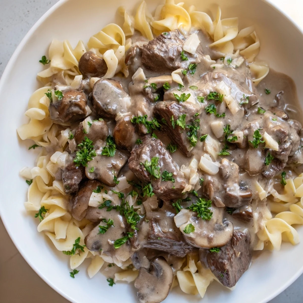 Hearty beef stroganoff in savory sour cream sauce plated over steaming egg noodles