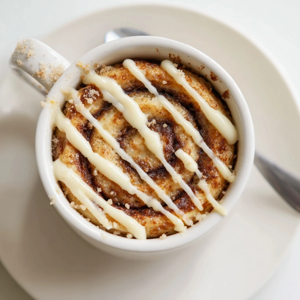 Warm cottage cheese cinnamon roll mug cake topped with cream cheese icing and cinnamon swirl