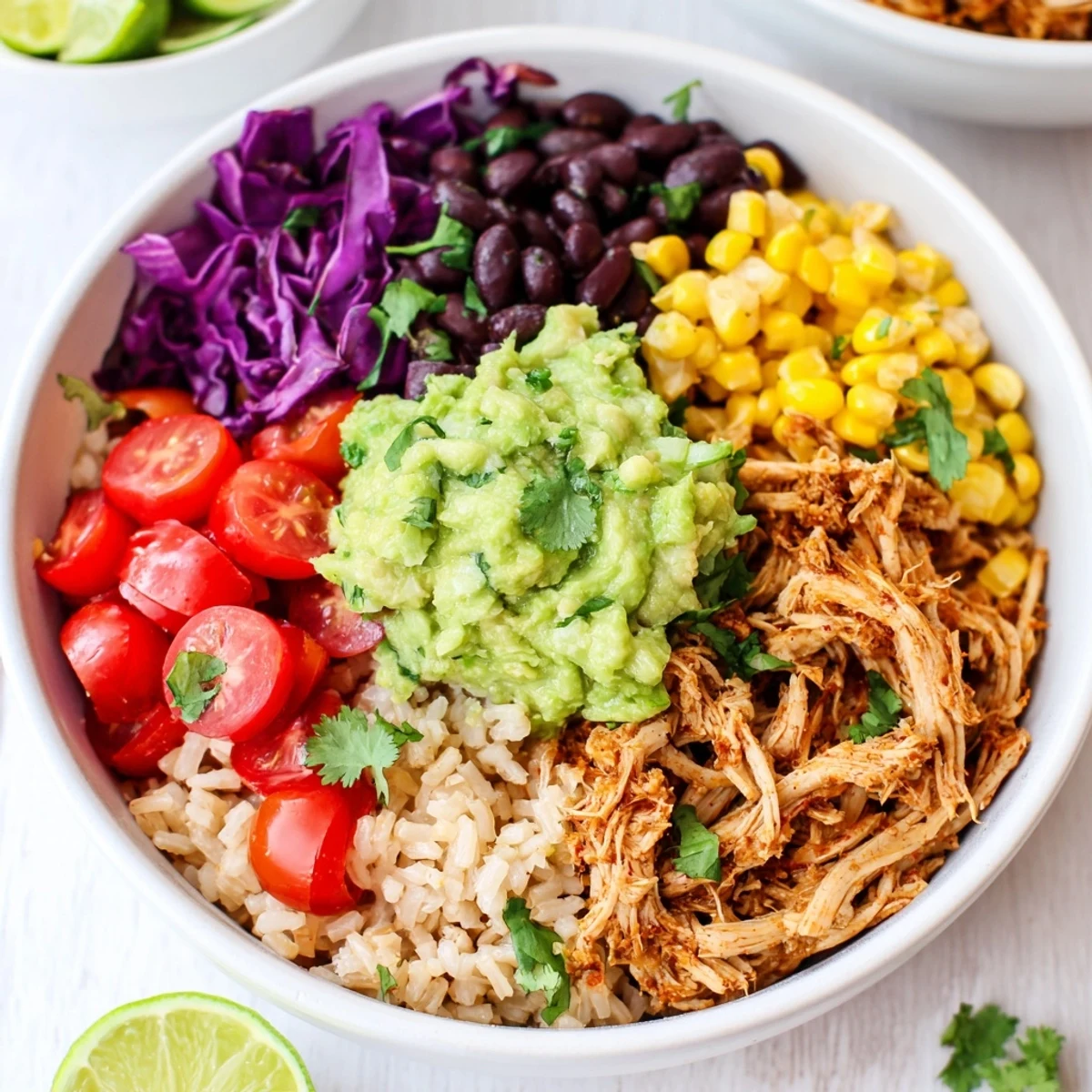 Vibrant pulled chicken guacamole bowl topped with fresh cilantro and lime wedges