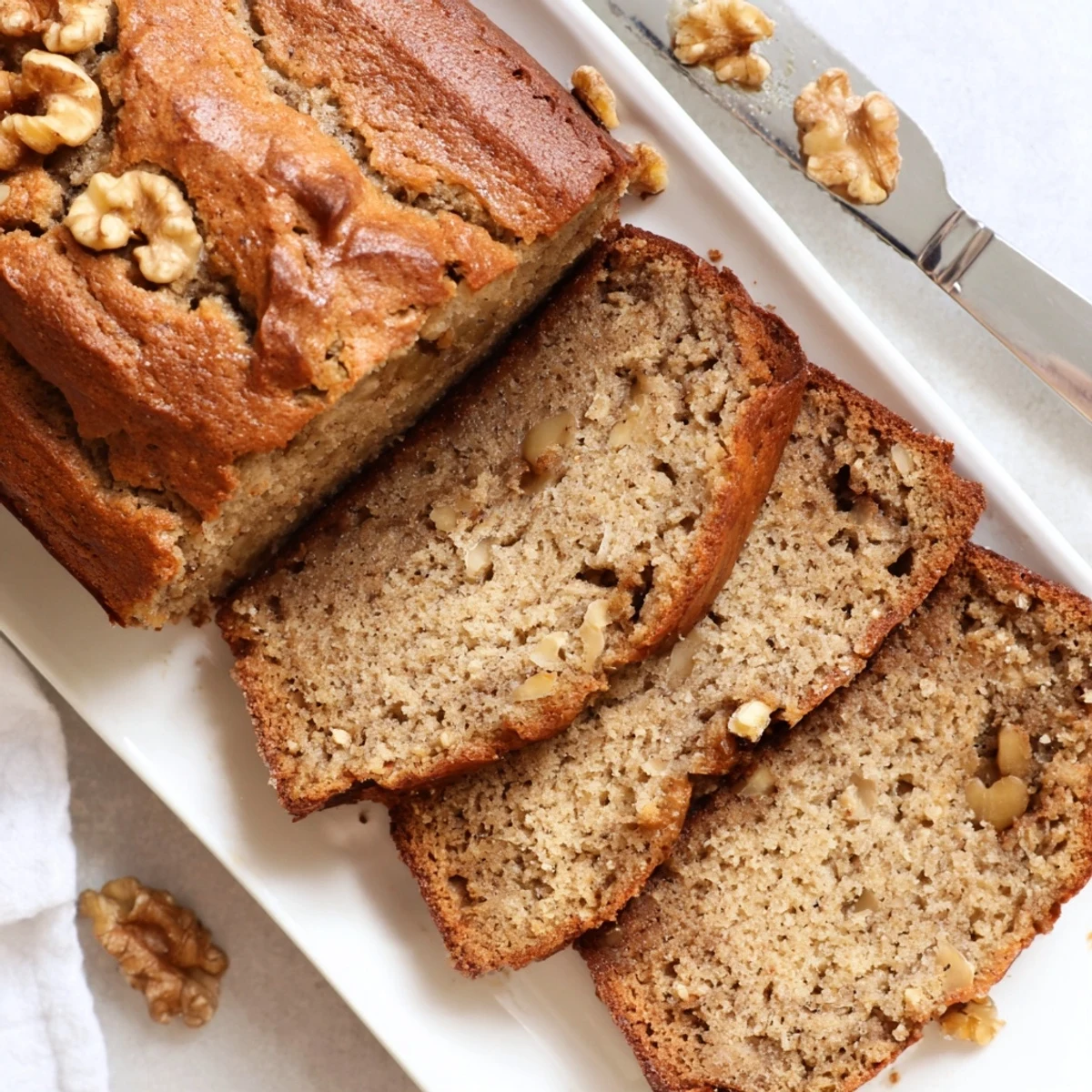 Golden brown keto banana bread loaf sliced on wooden board with walnuts