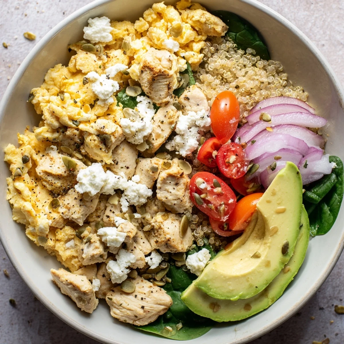 Protein-packed breakfast bowl topped with scrambled egg mixture, diced chicken, vegetables, and crunchy seeds