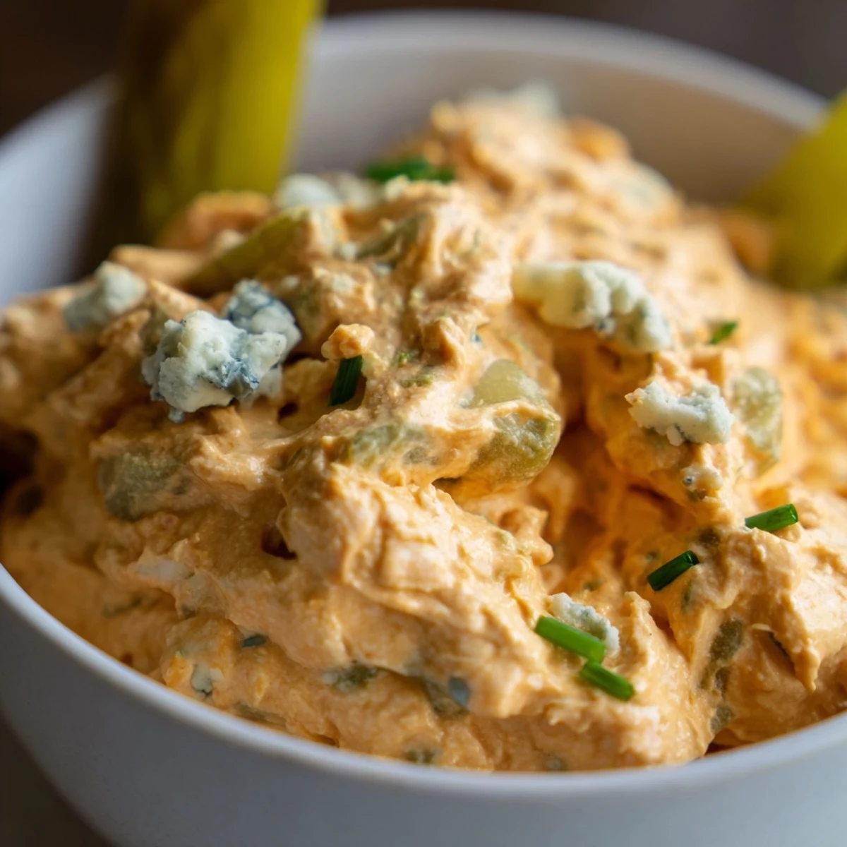 Creamy buffalo pickle dip in a serving bowl surrounded by crunchy chips and fresh veggie sticks