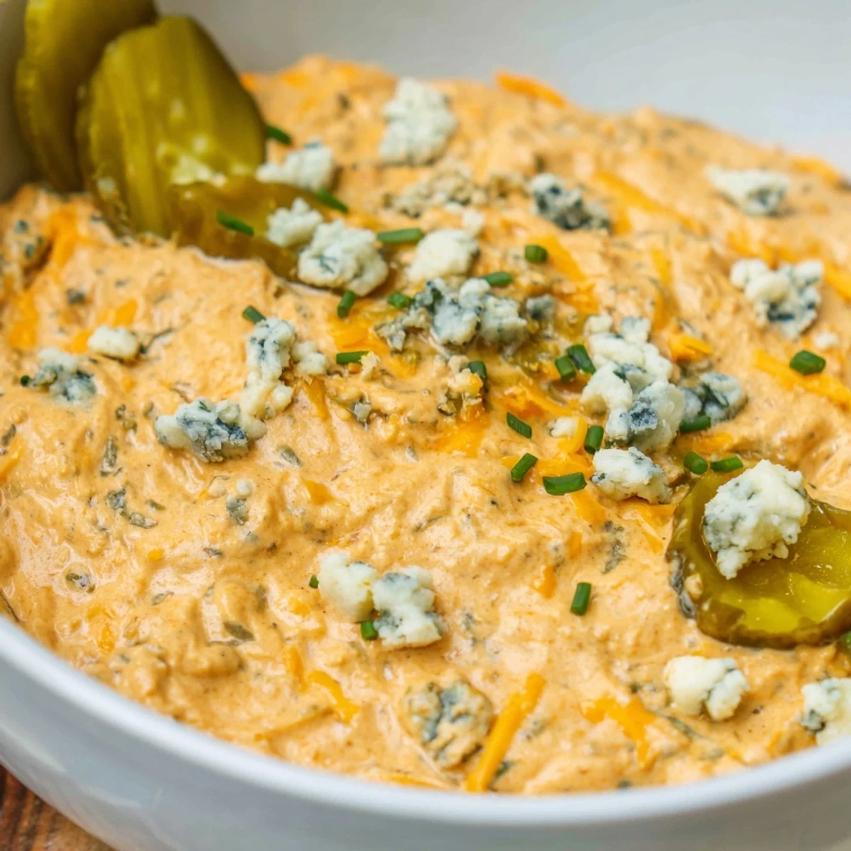 Tangy buffalo pickle dip topped with cheddar cheese and fresh chives in a rustic bowl