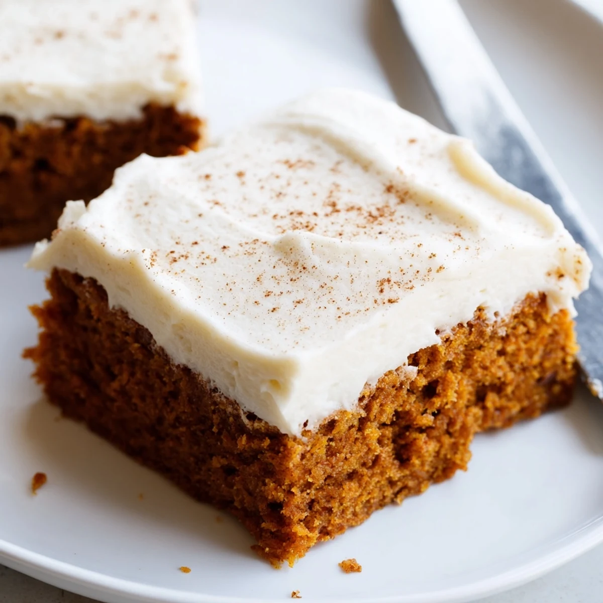 Golden pumpkin bars with cream cheese frosting sprinkled with cinnamon on a rustic plate