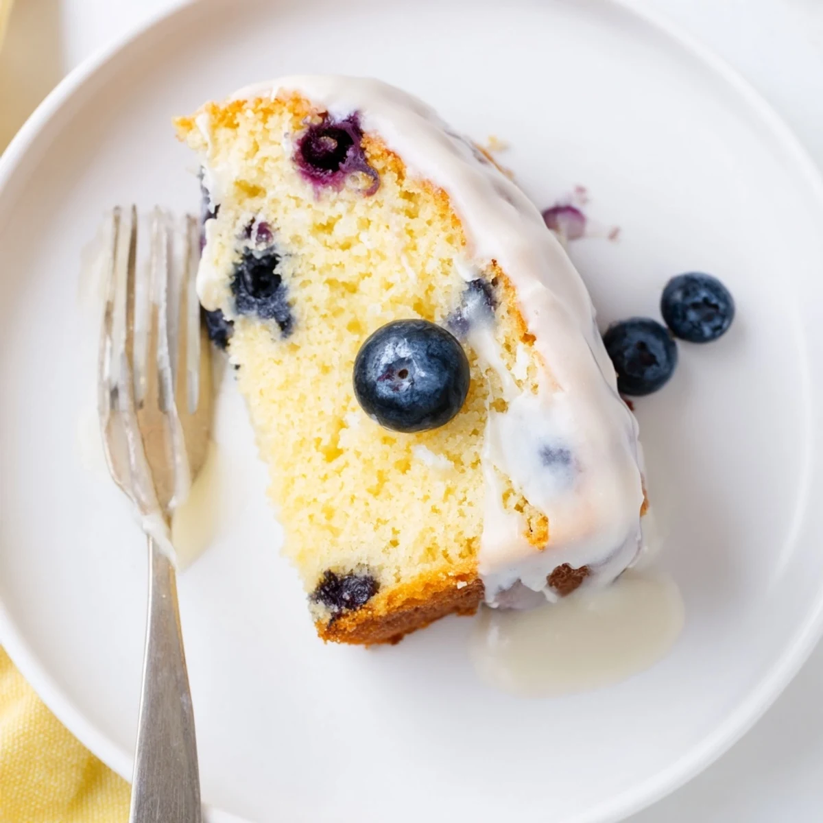 Homemade lemon blueberry cake on a white plate with zesty citrus garnish and dusting of powdered sugar