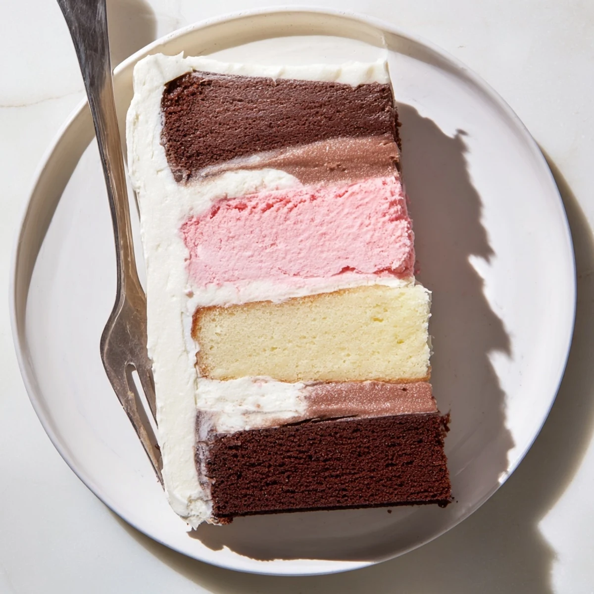 Slice of Neapolitan cake revealing chocolate, vanilla, and strawberry layers topped with creamy white buttercream