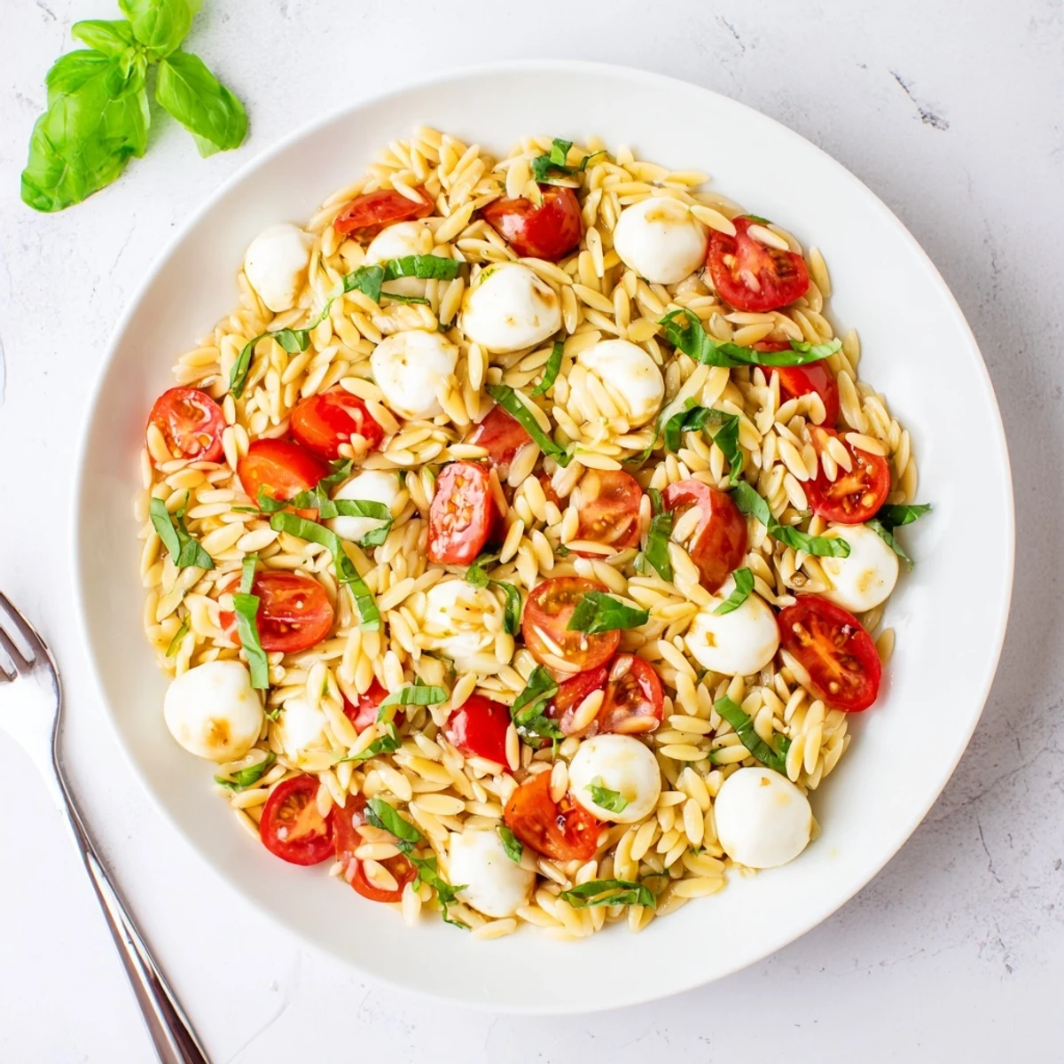 Vibrant Italian Caprese orzo pasta salad drizzled with balsamic vinaigrette and garnished with green basil leaves