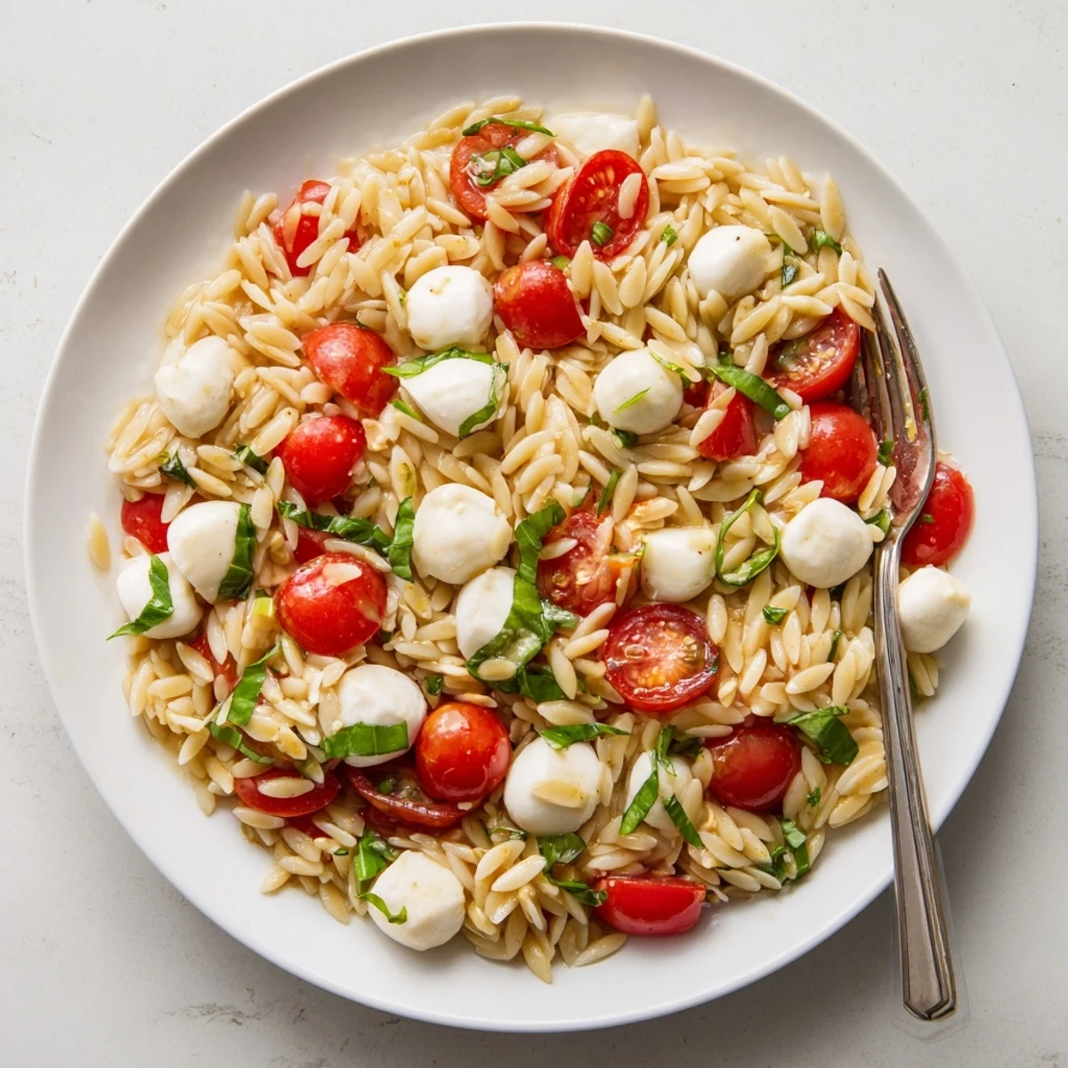 Colorful Caprese orzo pasta salad with juicy cherry tomatoes, fresh basil, and creamy mozzarella in a bowl