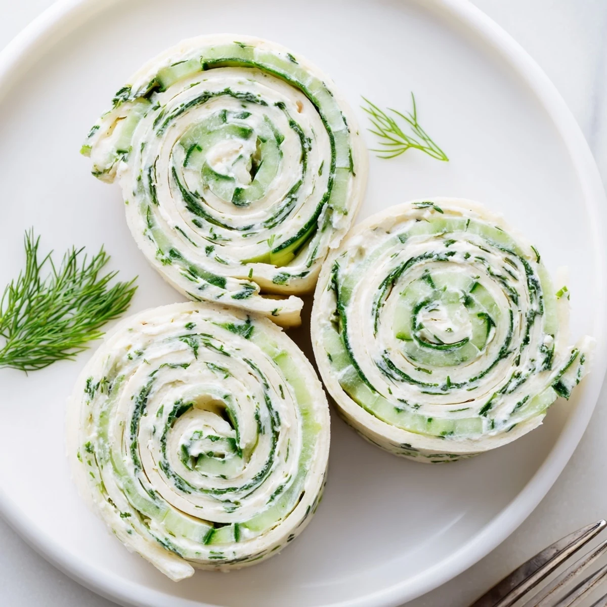 Chilled Cucumber And Dill Pinwheels on platter, creamy filling and crunchy cucumber