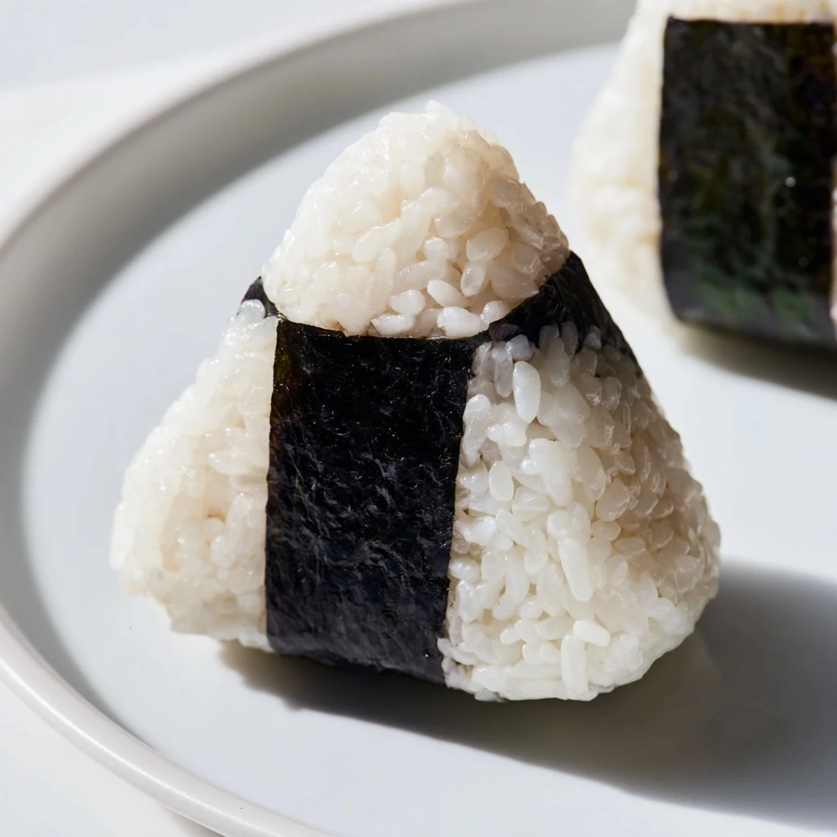 Golden triangular tuna mayo onigiri wrapped in crispy nori seaweed strips on a wooden board