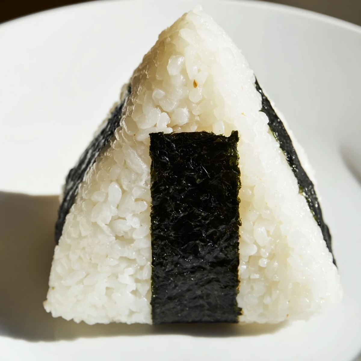 Handheld Japanese rice balls stuffed with creamy tuna mayonnaise filling, glistening under natural light