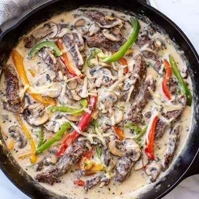The Creamy Keto Philly Cheesesteak Skillet bubbling in a cast iron pan, featuring sautéed mushrooms and onions in a rich sauce.