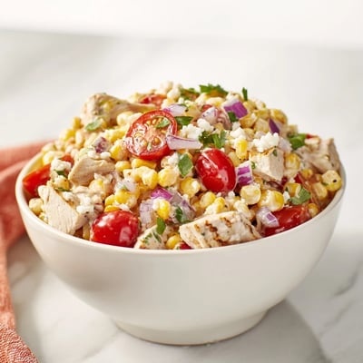 Bowl of grilled chicken street corn salad with charred corn, juicy tomatoes, and creamy dressing.